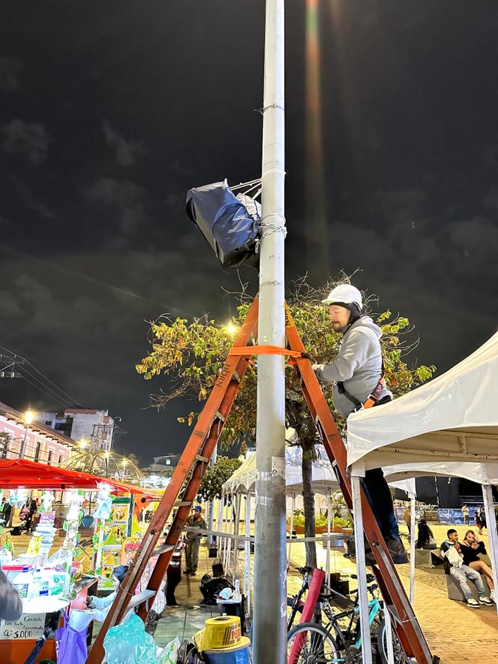 Dos cabinas de sonido en lo alto del mismo poste, apuntando a lados opuestos, con un técnico en la escalera