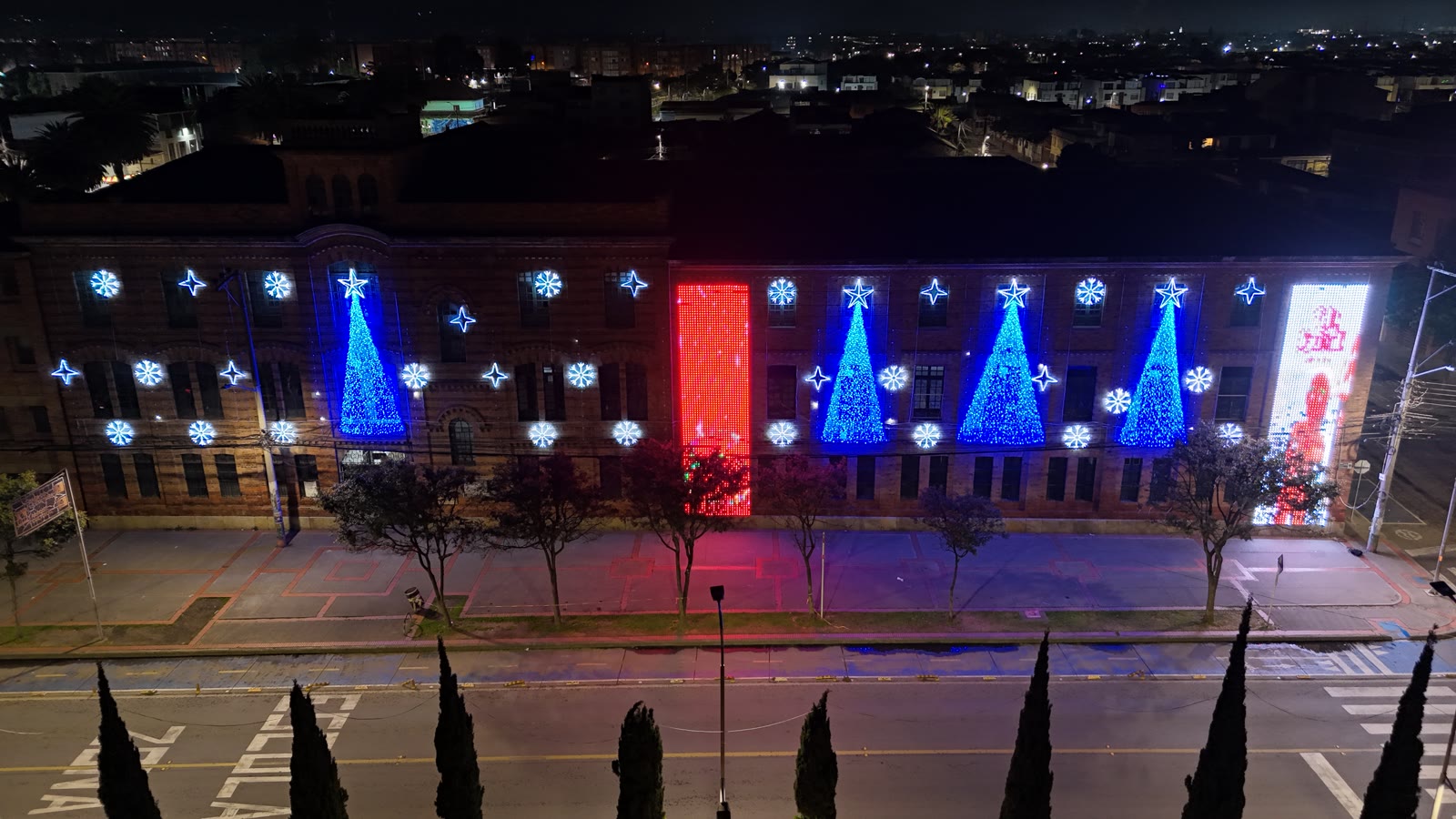 Fachada de tres pisos iluminada de noche, con dos secciones de pantalla LED verticales, una a cada lado del conjunto